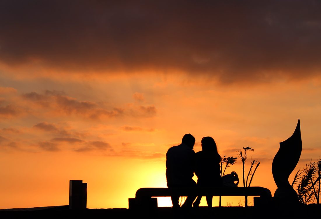A couple sit on a bench at sunset
