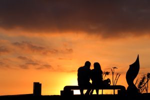 A couple sit on a bench at sunset